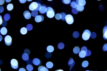 Defocused bokeh christmas cold lights on black background. Blue bokeh glitter wallpaper. Christmas theme, New year or festival background. Abstract blurred blue glitter texture.