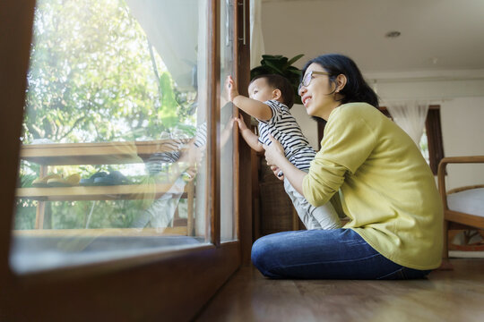 Beautiful Young Asian mother and Little son looking out the window at home.