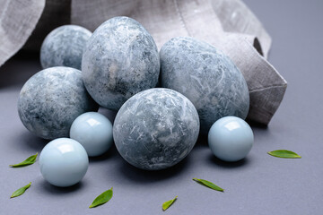 On a gray background, close-up marble-colored Easter eggs with green leaves and a linen napkin.