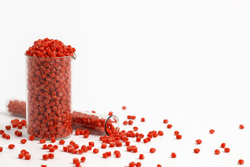 Red granules of polypropylene, polyamide in a measuring beaker and a test tube on a white background. Chemical products. Plastic, polymers and microplastics.