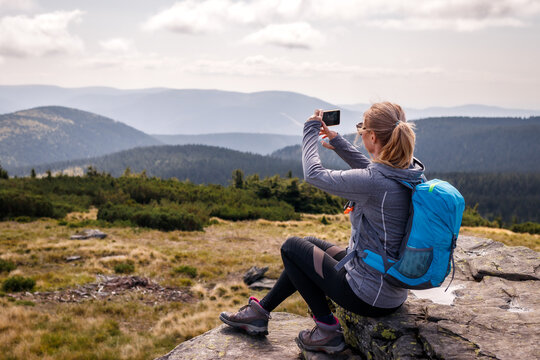 Woman hiker taking picture of mountains at her smart phone. Hiking vacation in nature