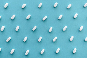 Blue medicine background with white scattered pills and tablet, macro. The concept of medicine, pharmacology and health.
