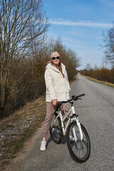 Fototapeta na wymiar young woman in sunglasses on a bicycle, on a road surrounded by trees without leaves, in spring with a clear blue sky