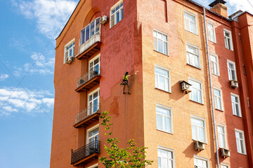 A painter climber is painting the building against the blue sky with white clouds