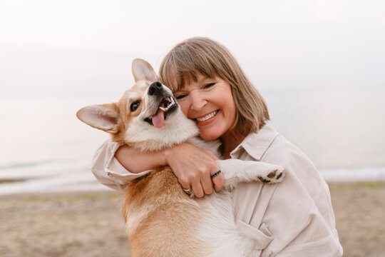 Senior Woman Laughing And Playing With Her Dog While Resting On Beach