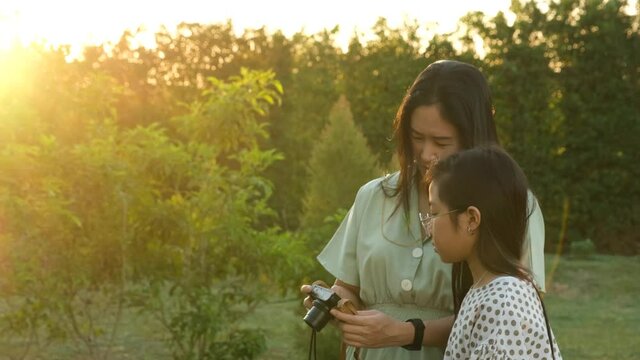 Asian mother and daughter look at photos from a compact camera in the garden where the sun's rays are pouring down to warm the atmosphere
