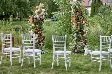 Place for wedding ceremony in garden outdoors, copy space. Wedding arch decorated with flowers. Wedding setting