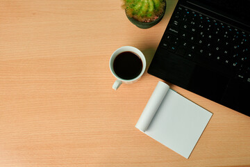 Top view of a keyborad, plant, coffee cup and blank paper on a wooden desk. Copy space