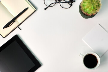 Top view of a tablet, coffee cup, a plant, notebook and glasses on a white background. Copy space