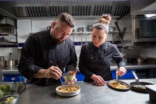 Male and female chefs garnishing savory dish in kitchen