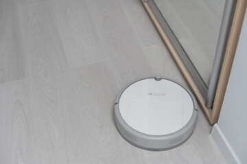 Robotic vacuum cleaner on laminate wood floor in bedroom.