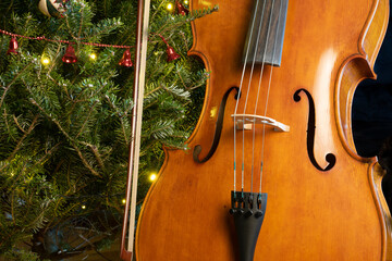 Fototapeta na wymiar Cello with a bow on Christmas tree background.