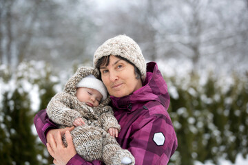 Grandmother holding little toddler boy outdoor on a snowy winter day