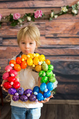 Fototapeta na wymiar Beautiful blond child, toddler boy, painting easter eggs with mother at home, making easter wreath