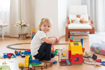 Cute child, playing with colorful toy blocks. Little boy building house of block toys sitting on the floor in sunny spacious bedroom