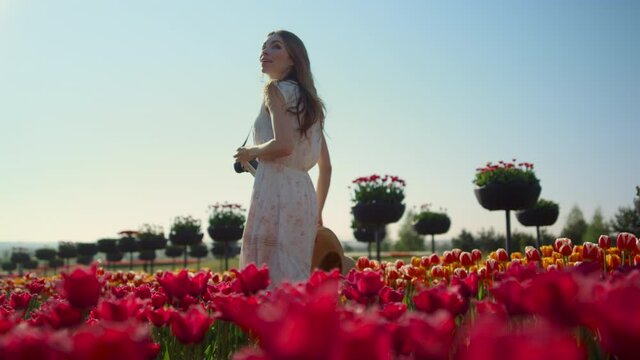 Beautiful girl with camera walking through tulip field. Woman smiling in garden.