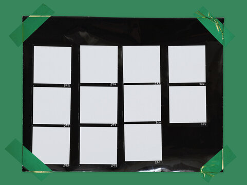 top shot photo of black and white hand copy contact sheet with 11 empty film frames fixed by green plastic sticker tape on green paper background. cool retro picture placeholder.