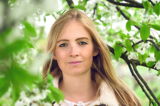 Portrait of a beautiful young woman in nature, with spring blossoms and tender green foliage on tree branches surrounding her face