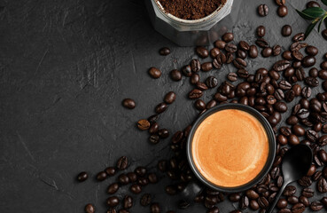 Espresso in a cup on a black table next to a coffee pot. Coffee beans and coffee ingredients on the table. Top view, place for text. Italian style breakfast idea.