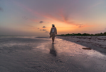 young hispanic woman from the back with a hat walking along the seashore at sunset on a caribbean island