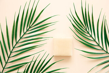 Natural handmade soap and palm leaves on a beige background, top view. Skin care and beauty...