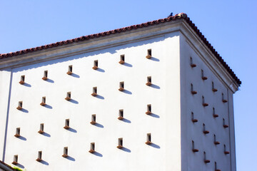 bird houses. many loopholes in white building with pigeon on the roof