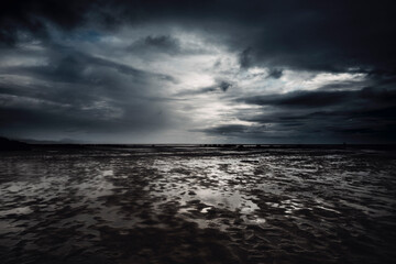 Dramatic cloudscape and flood beach in dark night weather. Stormy and rainy sky with ocean in background. Epic seascape with white sunset light and black clouds. - Powered by Adobe