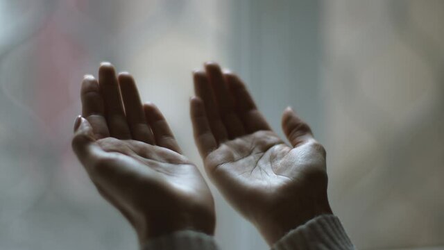 Close up shot of female palms against window, unrecognizable muslim lady praying to God, gesturing hands up, slow motion
