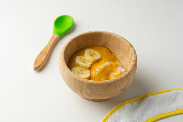 Wooden bowl of baby food, healthy breakfast porridge with banana. Bright background.