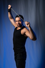 a muscular man holds a chain above his head. Black background