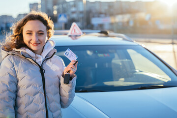 Proud young girl with car licence just after finishing driving school and getting drivers license with examination car on background.. Outdoor portrait.