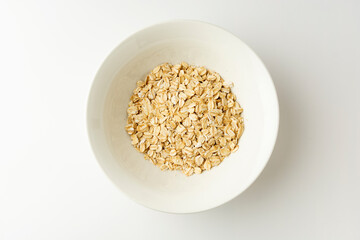 Rolled oats in a bowl on white background, top view