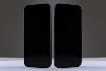 two black rectangular smartphones with glossy screens next to each other on a gray isolated background, concept mockup