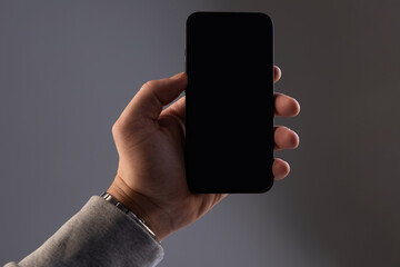 black rectangular modern smartphone he in a male hand on a gray isolated background, Concept mockup, smartphone screen with copy-space