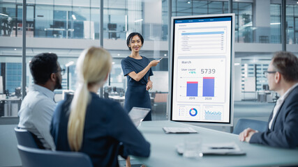 Female Operations Manager Holds Meeting Presentation for a Team of Economists. Asian Woman Uses Digital Whiteboard with Growth Analysis, Charts, Statistics and Data. People Work in Business Office.