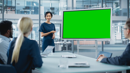 Female Operations Manager Holds Meeting Presentation for a Team of Economists. Asian Woman Uses Digital Whiteboard with Horizontal Green Screen Mock Up Display. People Work in Business Office.