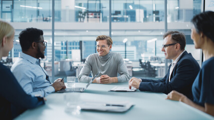 Modern Office Meeting Room: Handsome Executive Director Sits in the Head of the Conference Table and Delivers Strong Speech to a Group of Businesspeople and Talks with Investors.