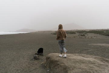 Young girl on the beach looking at the horizon with dog beside black.