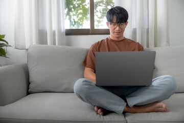 Naklejka premium Work at home young asian man working on laptop computer while sitting at home Morning lifestyle