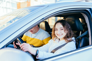 Laughing young woman in drivers seat of car taking driving lesson from instructor. Driving school concept.