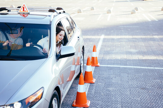 Driving school or test. Beautiful young woman with male instructor learning how to drive and parking car between cones. © Iryna