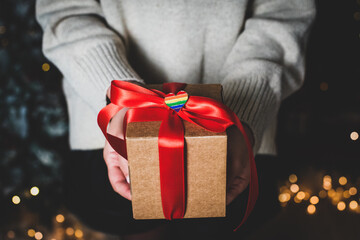 Woman holds gift with red ribbon and heart-shaped lgbt icon in hand. craft box and garland