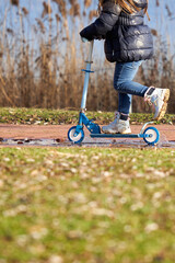 Obraz premium Girl riding scooter near lake. Child with blue sports equipment.