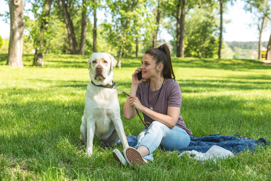 Young happy satisfied business woman taking a day off from work to enjoy with her white Labrador Retriever pet dog. Successful female spending time outdoor with her puppy friend.
