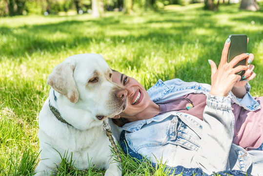 Young happy satisfied business woman taking a day off from work to enjoy with her white Labrador Retriever pet dog. Successful female spending time outdoor with her puppy friend. - Powered by Adobe