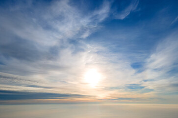 Obraz premium Aerial view of bright yellow sunset over white dense clouds with blue sky overhead.