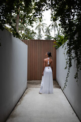 A tanned Thai woman in white dress poses at tropical view, Koh Samui, Thailand.