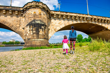Back view of woman walking along the city river with her daughter on a sunny day.