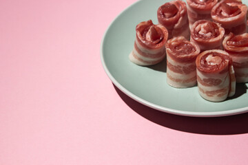 Bacon on a pink background. Raw bacon on a plate.  Pig meat. rolled bacon