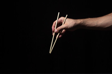 Hands holding Chinese chopsticks on a black background. Traditional wooden Chinese sticks.